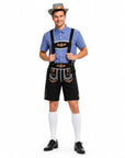 A man modeling a traditional Bavarian-style outfit consisting of a blue checkered shirt, black embroidered Lederhosen with gold accents, white knee-high socks, and a gray cowboy hat, against a plain white background.