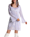 Woman wearing a white, shiny dress with funky 70s patterns on a white background