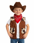 A young boy modeling a brown faux-suede cowboy costume vest with camouflage-patterned patches, a matching brown cowboy hat, and a red bandana, worn over a white t-shirt and blue jeans against a white background.