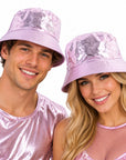 A man and a woman wearing shiny metallic pink bucket hats and matching pink tops, smiling against a plain white background.