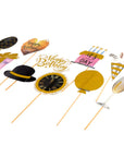 A set of birthday party photo booth props on wooden sticks, including a black top hat with a gold band, a gold balloon, a black clock face, a pink cake, a champagne glass, and other festive shapes, all displayed on a clean white background.