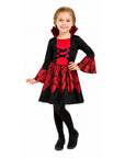A young girl modeling a vampire costume dress with black and red fabric, featuring a ruffled collar, lace-up chest detail, patterned skirt, and black tights against a plain white background.