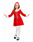 A young girl modeling a red and white Santa Claus costume dress with white tights and black Mary Jane shoes, posed against a solid white background.