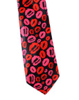 A necktie featuring a repeating pattern of red and hot pink lipstick kiss marks on a black background, shown against a plain white studio backdrop.