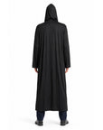 A person viewed from the back wearing a long black hooded robe or cloak over dark pants and black shoes, standing against a plain white studio background.