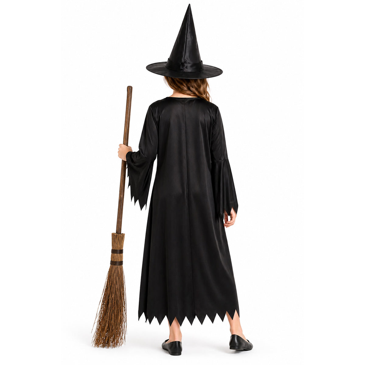 A child shown from the back wearing a black witch costume with a pointed black hat and holding a brown broom against a plain white studio background.