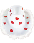 A white cowboy hat with a fluffy white faux-fur trim and scattered red glitter hearts, shown against a plain white background.