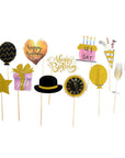 A set of 12 birthday party photo booth props on wooden sticks, featuring gold, black, pink, and white designs including a star, gift box, hat, cake, champagne flute, and balloons.