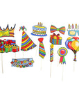 A set of colorful birthday photo booth props on sticks, including a crown, party hat, cake, bow tie, glasses, balloons, gifts, ribbon, and a banner, shown against a plain white background.